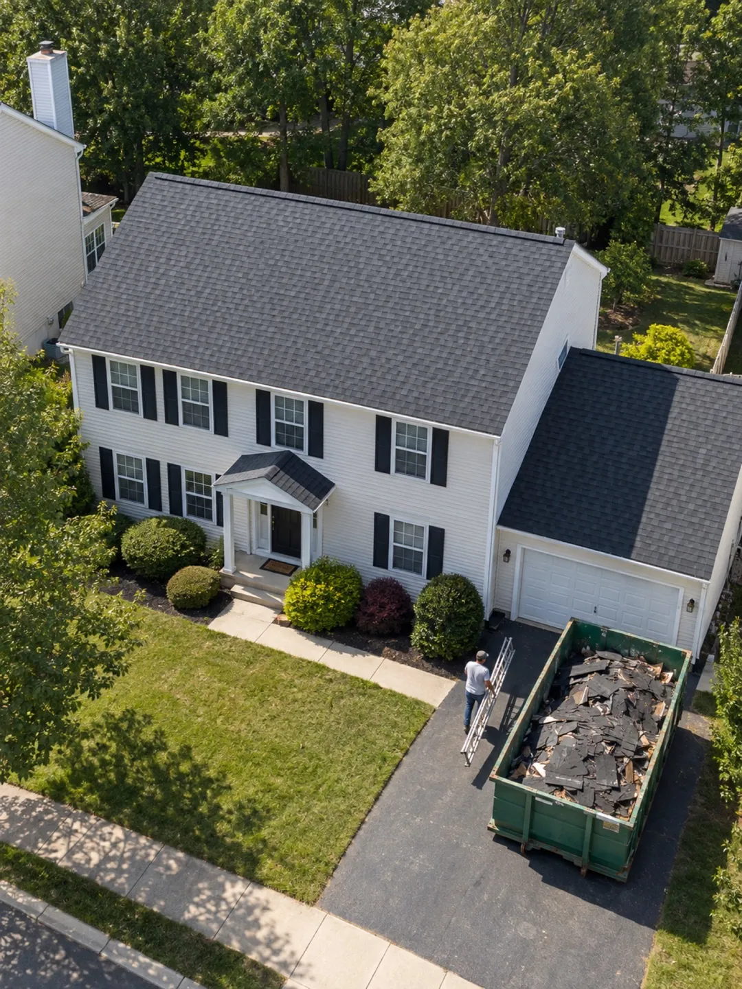 A Titan East crew finishing a new gray roof, with the old shingles in a dumpster in the driveway